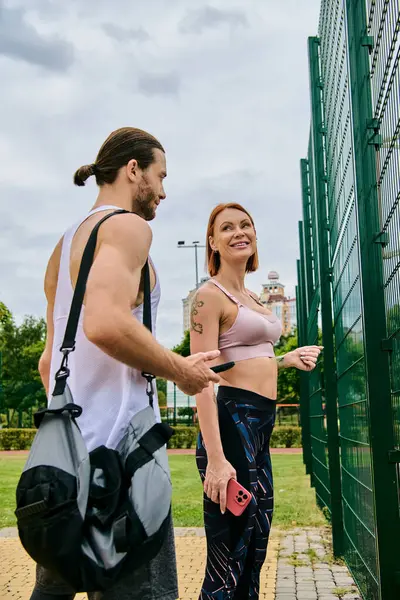 Un hombre y una mujer decididos en ropa deportiva se paran junto a una valla después del entrenamiento - foto de stock