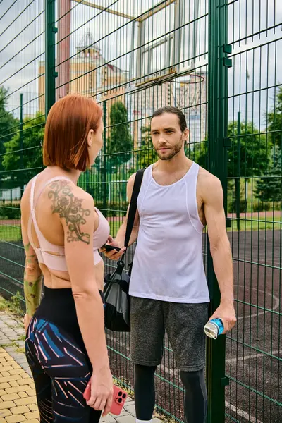 Un hombre y una mujer decididos en ropa deportiva se paran juntos al aire libre por una valla, - foto de stock