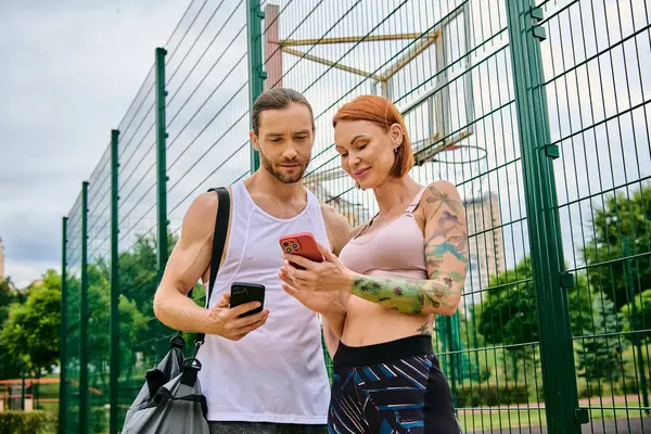 Un hombre y una mujer en ropa deportiva, comprobar su progreso en un teléfono celular. - foto de stock