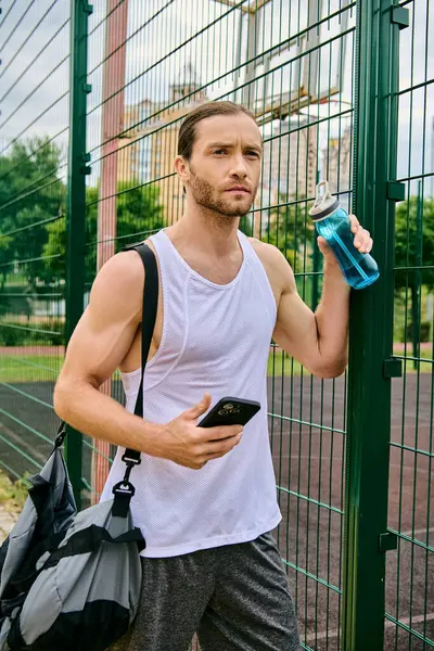 Ein Mann steht neben einem Zaun und hält ein Handy in der Hand, vertieft in seinen Inhalt.. — Stockfoto