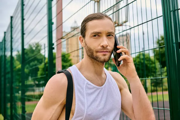 Un hombre decidido en ropa deportiva habla en su teléfono celular en un entorno al aire libre mientras muestra su fuerza y concentración. - foto de stock
