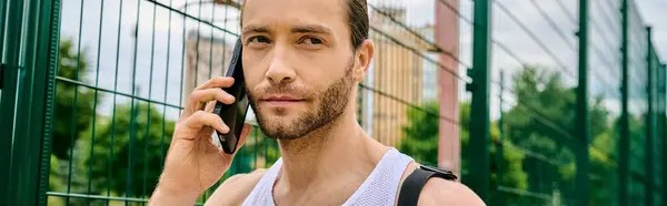 Un hombre en una camiseta sin mangas se involucra en una conversación telefónica después de una sesión de entrenamiento al aire libre - foto de stock