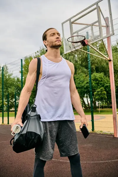 Un uomo determinato in abbigliamento sportivo si trova su un campo da basket in possesso di una borsa, pronto per la sua prossima sessione di allenamento — Foto stock