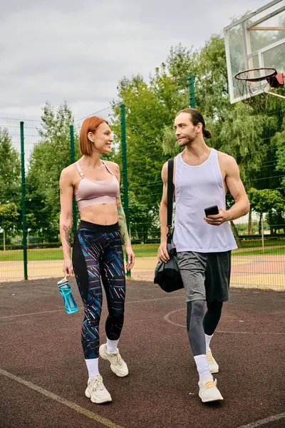 Un hombre y una mujer decididos en ropa deportiva caminan juntos en una cancha de baloncesto - foto de stock