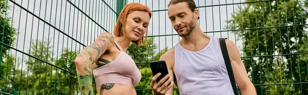 A man and woman in sportswear stand together outdoors, using smartphone — Stock Photo
