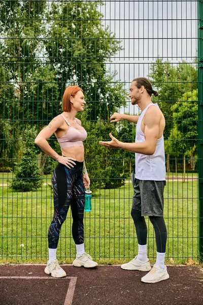 Un uomo e una donna, in abbigliamento sportivo, a chiacchierare davanti a una recinzione. — Foto stock
