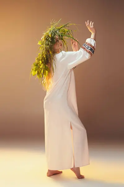 Una giovane donna in un abito bianco adorna la sua testa con una corona di piante, incarnando un'estetica stravagante, simile a una fata in un ambiente da studio. — Foto stock