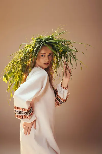 Une jeune mavka embrassant la nature, revêtue d'une robe blanche ornée, avec une plante délicatement perchée sur sa tête dans un décor de studio. — Photo de stock