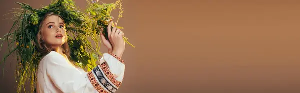 Jeune mavka en robe blanche tient délicatement un bouquet de plantes vertes dans un décor de studio de fées et de fantaisie. — Photo de stock