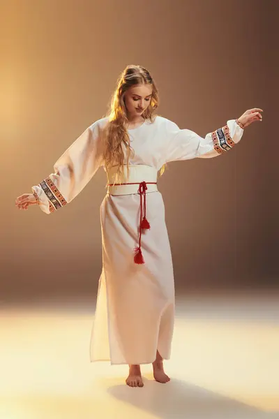 Une jeune mavka orne gracieusement une robe blanche traditionnelle avec un pompon rouge frappant, créant une ambiance de conte de fées dans un cadre de studio. — Photo de stock