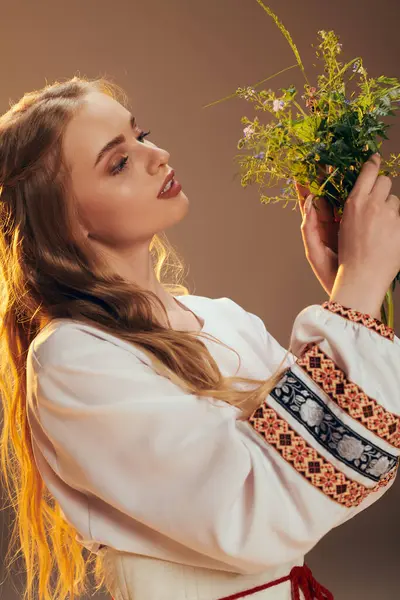 Une jeune femme en robe blanche tenant gracieusement un bouquet de fleurs dans un décor studio magique. — Photo de stock