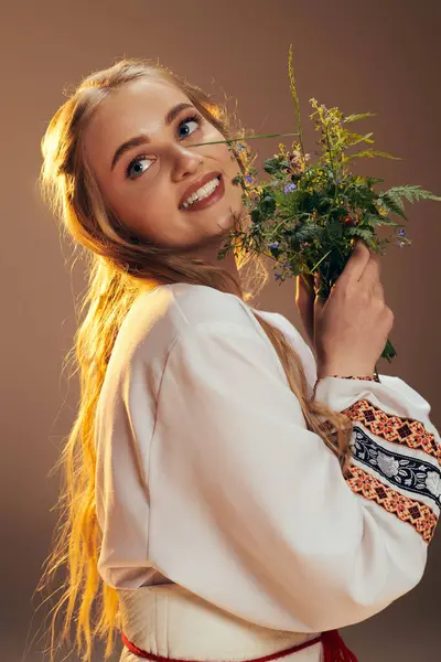 Une jeune mavka en robe blanche tient gracieusement un bouquet de fleurs dans un décor de studio fantastique. — Photo de stock