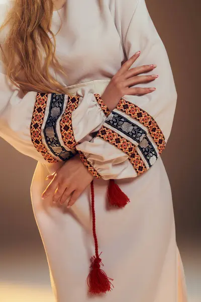 Eine junge Mavka in einem atemberaubenden weißen Kleid, geschmückt mit einer leuchtend roten Quaste, verkörpert eine märchenhafte Präsenz in einem Studio-Setting. — Stockfoto