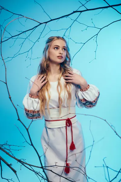 Молода жінка в білій сукні витончено стоїть перед величним деревом, втілюючи казкові та фентезійні елементи в обстановці студії. — стокове фото