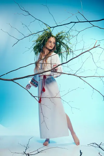 Молода мавка в білій сукні делікатно тримає гілку дерева в фантастичній студії. — стокове фото