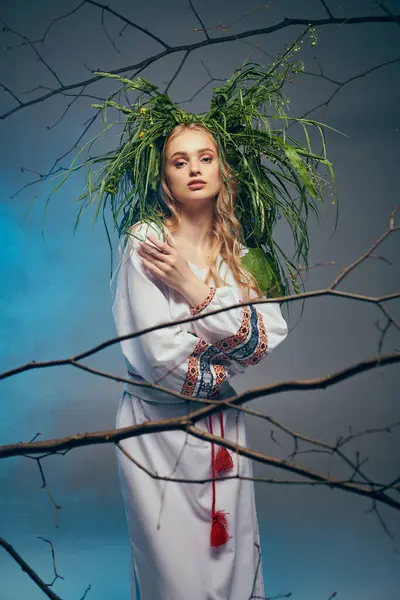Молода жінка в традиційному вбранні витончено стоїть перед величним деревом, прикрашеним вінком на голові. — стокове фото