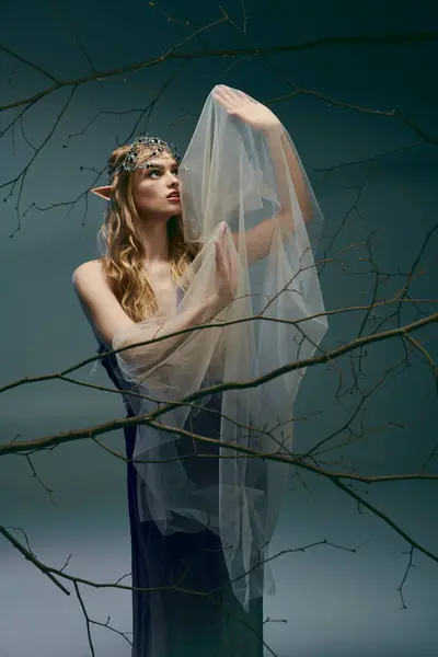 Молодая женщина, одетая как принцесса эльфов, грациозно стоит перед величественным деревом в вуали. — стоковое фото