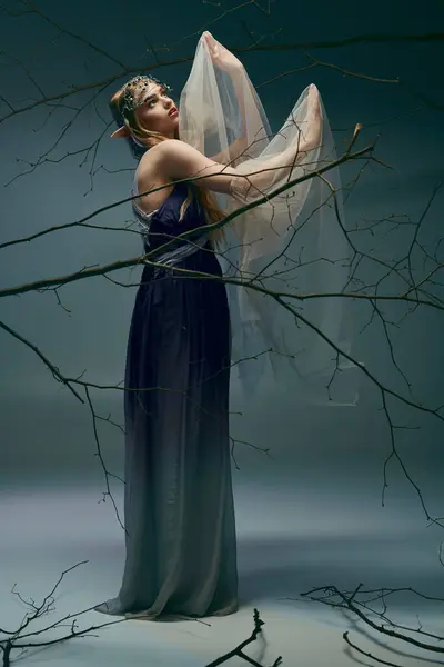 Uma jovem mulher em um vestido longo está delicadamente segurando um véu, exalando uma aura de fada em um estúdio. — Fotografia de Stock