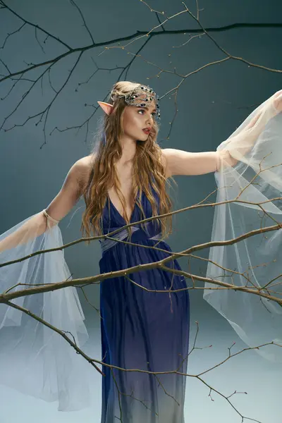Молодая женщина в синем платье, элегантно стоящая перед величественным деревом, источающая ауру фей и фантазий. — стоковое фото