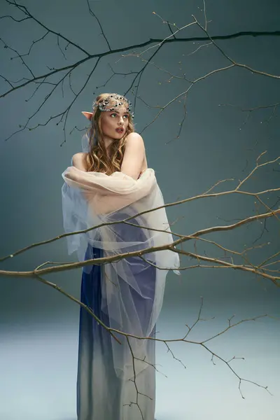 Una joven con un vestido azul de pie con gracia frente a un majestuoso árbol, encarnando la esencia de una princesa de hadas. - foto de stock