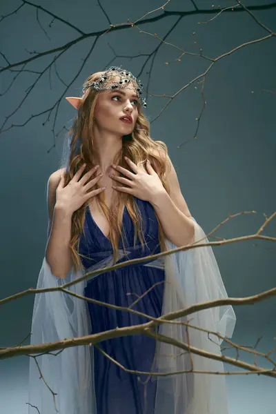 Uma jovem mulher em um vestido azul fica graciosamente ao lado de uma árvore majestosa em um cenário de conto de fadas. — Fotografia de Stock