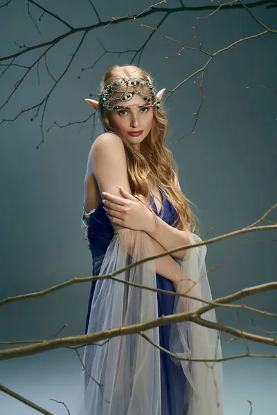 Молодая женщина в синем платье, воплощающая сущность сказочного персонажа, грациозно стоит у большого дерева. — стоковое фото