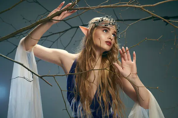 Una joven vestida con un vestido azul fluido se levanta con gracia junto a un árbol en un entorno de fantasía mágica. - foto de stock