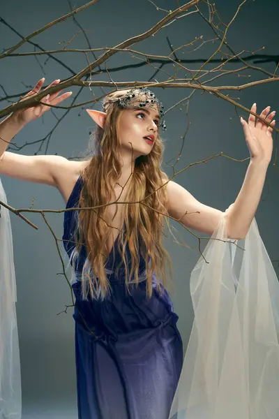 Молодая женщина в синем платье, грациозно держащая ветку дерева, воплощающая сущность феи-принцессы в мистической обстановке. — стоковое фото