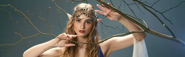 Uma jovem mulher em uma coroa fica graciosamente na frente de uma árvore majestosa em um cenário de fantasia, incorporando a essência de uma princesa elfo. — Fotografia de Stock