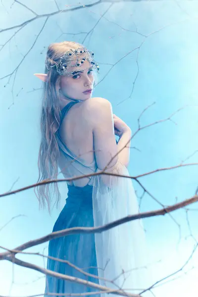 A young woman in a flowing blue dress stands gracefully in a tree, embodying a fairy princess in a fantasy world. — Stock Photo
