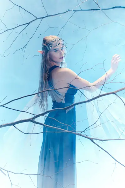 Eine junge Frau in einem blauen Kleid steht anmutig in einem Baum und verkörpert das Wesen einer Märchenprinzessin in einem mystischen Wald. — Stockfoto