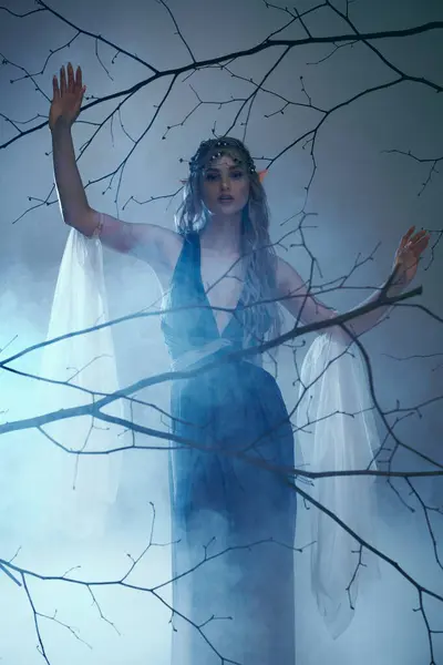 Une jeune femme dans une robe bleue fluide se tient gracieusement devant un arbre majestueux, incarnant l'essence d'une princesse fée. — Photo de stock