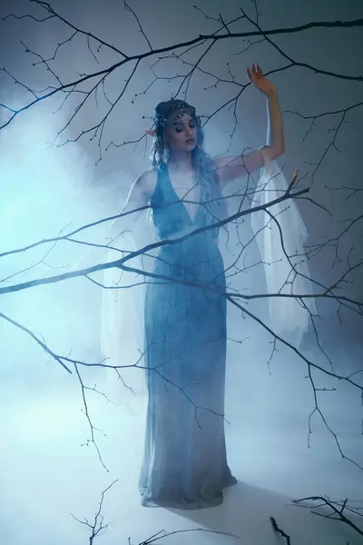 Eine junge Frau in einem blauen Kleid steht anmutig in einer nebligen Umgebung und verkörpert das Wesen einer märchenhaften Elfenprinzessin. — Stockfoto