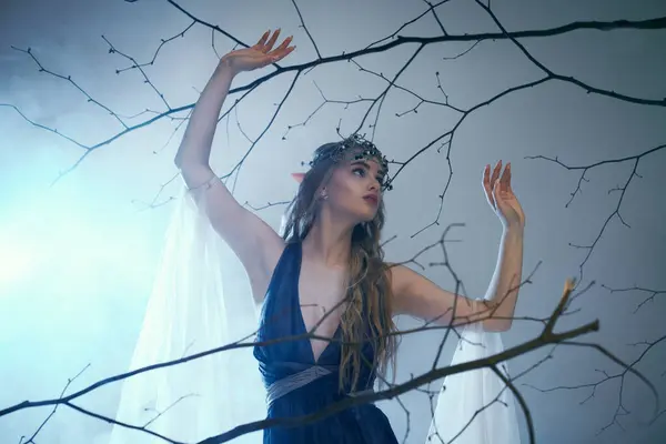 Uma jovem mulher em um vestido azul de pé graciosamente na frente de uma árvore majestosa, exalando um ar de fantasia e magia. — Fotografia de Stock