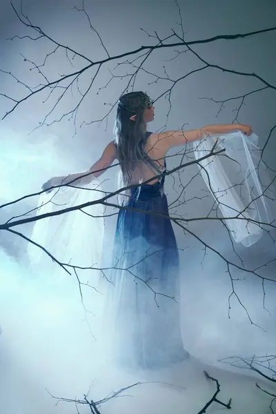 Молодая женщина в синем платье стоит в туманном лесу, воплощая сказочного персонажа или эльфийскую принцессу. — стоковое фото