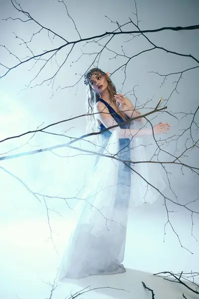 Молодая женщина в белом платье, похожая на принцессу эльфов, грациозно стоит перед величественным деревом в сказочной обстановке. — стоковое фото