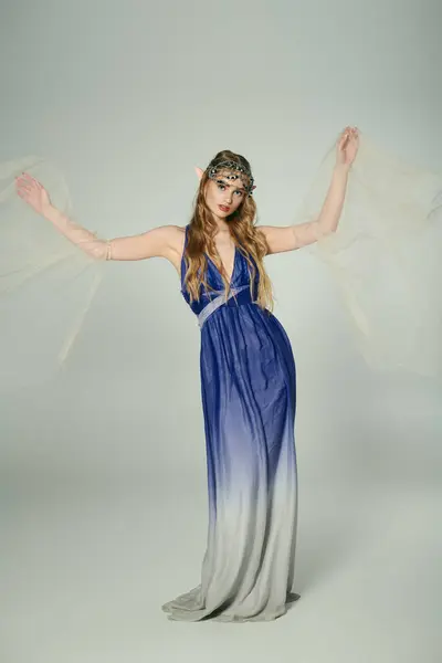 Eine junge Frau steht elegant in einem Atelier, in einem wunderschönen blau-grauen Kleid, das für eine Märchenprinzessin geeignet ist.. — Stockfoto
