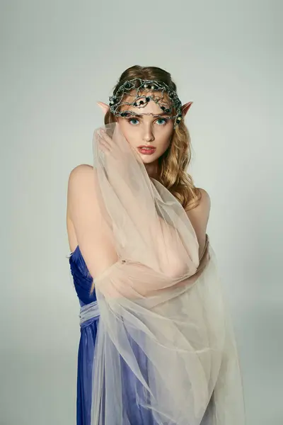 Eine junge Frau in einem blauen Kleid mit Schleier auf dem Kopf, verkörpert das Wesen einer mystischen Elfenprinzessin in einem skurrilen Studio-Setting. — Stockfoto