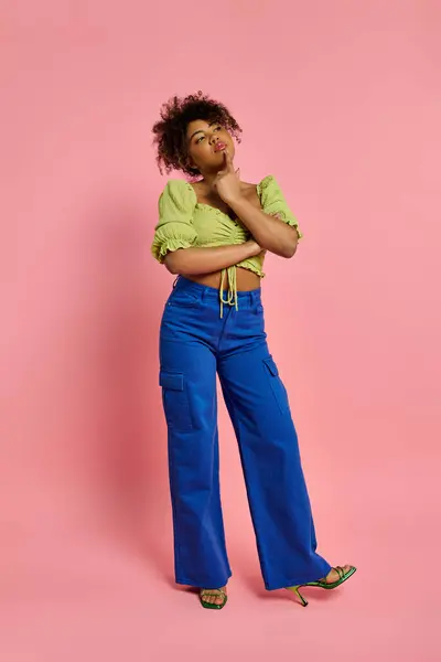 Красива афроамериканська жінка в жовтій сорочці і блакитних штанях позує на яскравий фон. — стокове фото