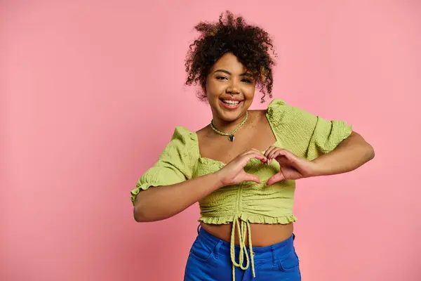 A beautiful African American woman in stylish attire making a heart shape with her hands against a vibrant backdrop. — Stock Photo