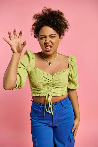 Uma bela mulher afro-americana emocional posando em um top amarelo elegante e calças azuis contra um cenário vibrante. — Fotografia de Stock