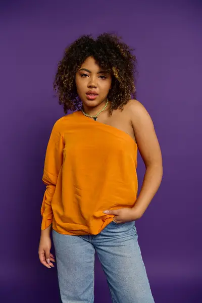 Elegante mujer afroamericana posa elegantemente en la vibrante parte superior naranja. - foto de stock