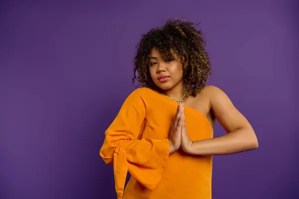 Stylish African American woman posing in orange top against vibrant purple backdrop. — Stock Photo