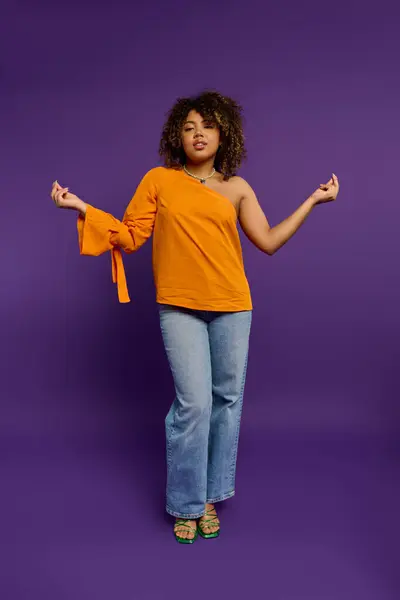 Афроамериканка в оранжевом топе позирует со стилем на ярком фоне. — стоковое фото