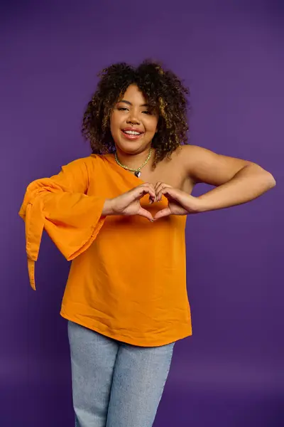 Stylish African American woman in front of vibrant purple background making heart with hands. — Stock Photo
