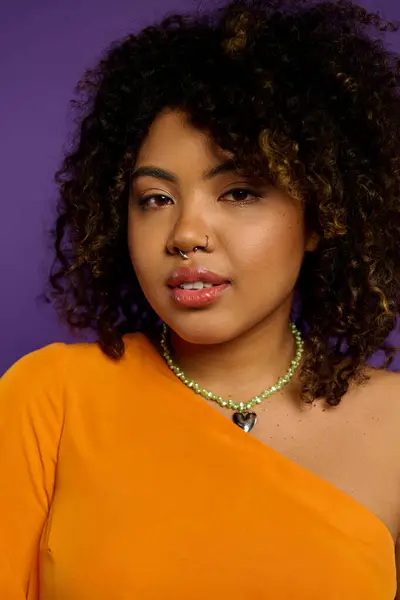 Beautiful African American woman in orange top and necklace poses against vibrant backdrop. — Stock Photo