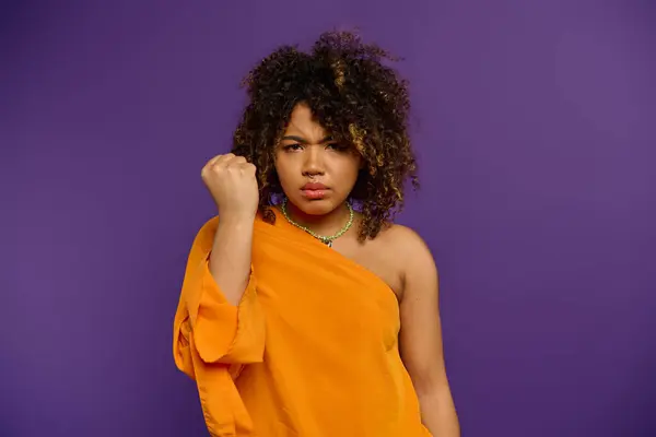 Stylish African American woman strikes a pose in an orange dress on a vibrant backdrop. — Stock Photo