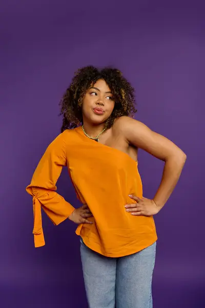 A beautiful African American woman with emotional expression poses stylishly in an orange top against a vibrant backdrop. - foto de stock