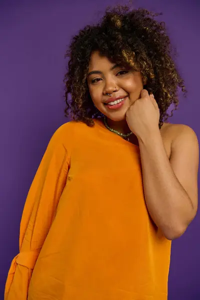 Stylish African American woman posing in an orange shirt against a vibrant backdrop. — Stock Photo