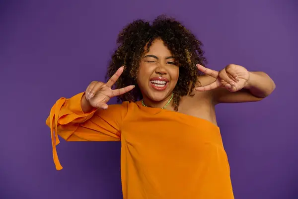 African American woman in orange top strikes a peace sign gesture. — Stock Photo